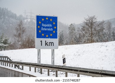 Snow is falling around a sign for European border, frontier between Germany and Austria. The sign says: 