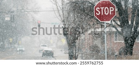 Snow falling in winter on street with stop sign and trees cars driving