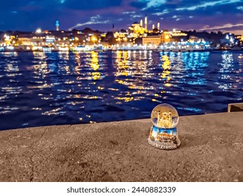 Snow globe of Istanbul on the backdrop of a blurred night landscape of Istanbul with evening lights. Tourist souvenir on the shore of the Golden Horn Bay with a reflection of the city in the water
 - Powered by Shutterstock