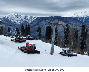 Snow groomers on a snowy mountain slope in a background of blue cloudy snow-capped mountains under the ski lifts, ski resort - Powered by Shutterstock