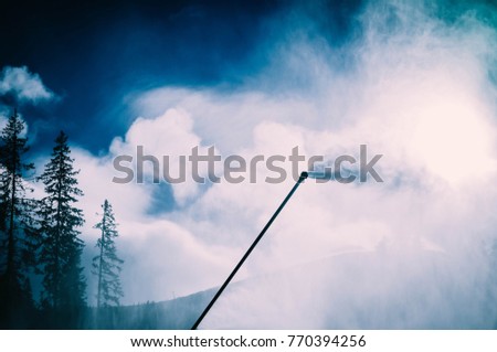 Snow gun, snow making process on a ski slope. Climate control with snowcannon on a ski resort, artificial snow spray on a mountains.