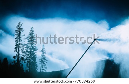 Snow gun, snow making process on a ski slope. Climate control with snowcannon on a ski resort, artificial snow spray on a mountains.
