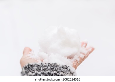 Snow hand close-up. A woman's hand in a gray sweater holds a lump of snow in the bright sunlight. The concept of cold winter snowfall, weather changes. Fabulous mood, snowball fight time on the street