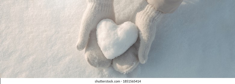 Snow heart in hands. Human hands in warm beige gloves with snowy heart against snow background. I love winter or St.Valentine's Day romantic creative concept. Panorama banner with free space for text