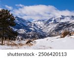 Snow in the high country in the Colorado Rockies.  Trees and snow in the foreground of the mountains of Colorado.  Pockets of snow and drifts in Moraine Valley. Rocky Mountain Natl Park. Blue sky.