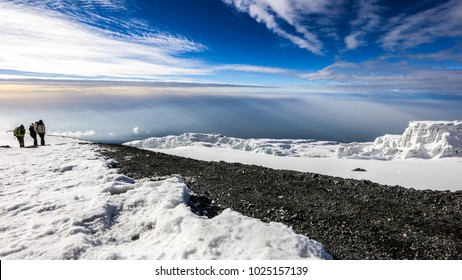 Snow, Ice And Glaciers On Top Of Mount Kilimanjaro At Sunrise With Clouds In The Sky Background And People Climbing To Summit, Africa