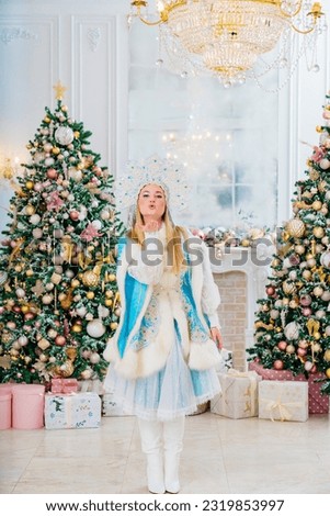 Snow Maiden in a blue traditional costume with a kokoshnik sends an air kiss in a room with christmas tree. The concept of Russian New Year's traditions. Congratulations to children.