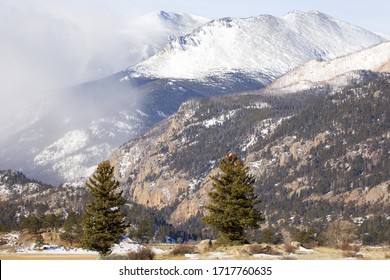 Snow melting in lower elevations as a snow squall comes to higher elevations in Colorado.  Trees in the foreground of the Rocky Mountains.  Pockets of snow surrounded by dormant vegetation.  