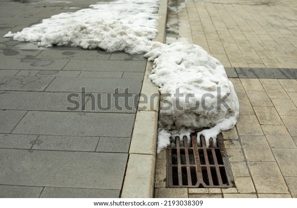 Snow melts at sewer grate. Removal of melt\
water from street. Sewer grate in\
city.