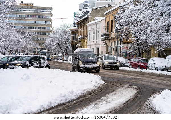 Snow on cars in the morning. Winter season and icy\
cars on the road in morning rush hour traffic of Bucharest,\
Romania, 2020
