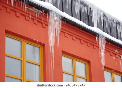 Snow on roof, huge icicles above the entrance. Dangling icicles put pedestrians in danger. Ice dams on residential building. 