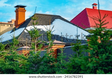 Snow on the tiled roof of a house melts on a clear sunny day. Thawing, winter scene.Spring landscape.