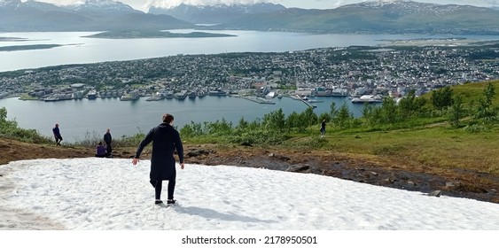 Snow On The Top Of The Mount Storsteinen In Summer And Panoramic View Of Tromso City In Norway. Man Slides Down From Snowy Mountain In Tromso, Norway.