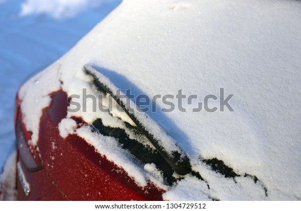 Snow on top of the rear glass\
of a red car. Photographed under daylight during winter in\
Finland.