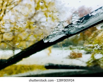 Snow On Windsheild Wipers With Yellow Autumn Leaves On The Tree In The Background