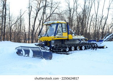 A snow plougher of ski trails stands on a platform near the forest on a winter day
