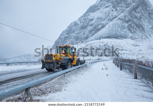 Snow ploughing truck cleaning snow on\
the road in suburban during heavy snowstorm\
falling