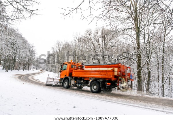 Snow\
ploughing truck cleans the country road leading through the  forest\
during a snowfall. Dangerous road\
conditions.