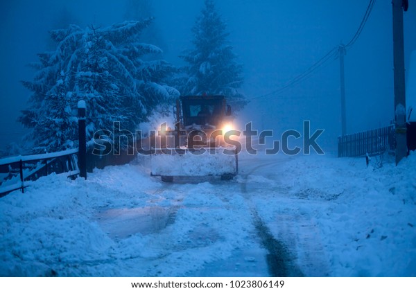 A snow\
plow clearing a road in winter, early\
morning