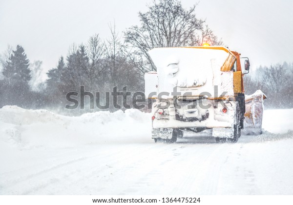 Snow plow / gritter cleaning road during heavy\
winter snow storm