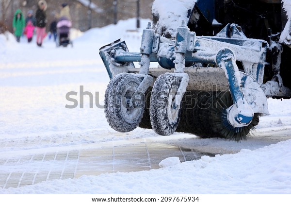 Snow plow machine\
removing the snow on the street on people background. Snowfall in\
winter city, frost weather