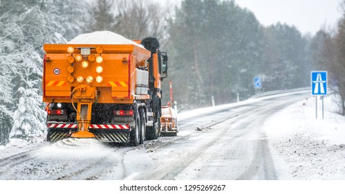 Snow Plow On Highway Salting Road. Orange Truck Deicing Street. Crystals Dropping On Snowy Asphalt. Maintenance Winter Vehicle In Action.