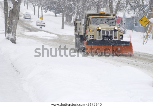 A snow plow in\
plowing a residential street.