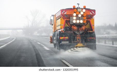 Snow Plow Salting Street In Winter Time. Orange Truck Deicing. Maintenance Winter Vehicle Back Side.  Focus On Front.