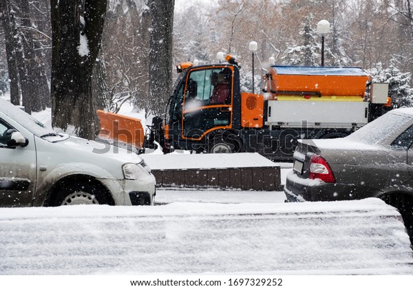 Snow plow is sprincling salt or\
de-icing chemicals on pavement in city. Cleaning service. Frost\
winter season. Winter anti-slip road handling\
concept.