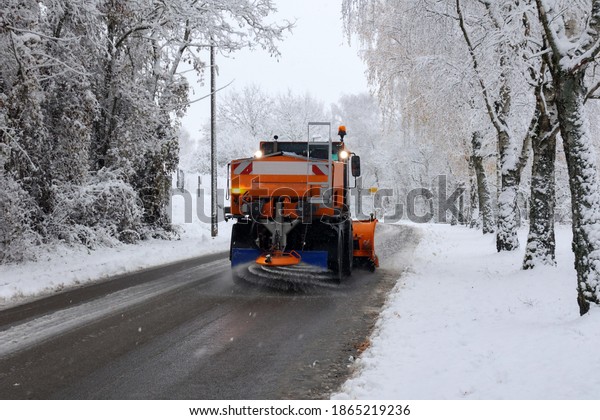 Snow plow is sprincling salt or de-icing chemicals\
on pavement in city.