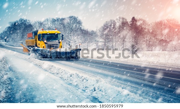 Snow plow truck cleaning snowy road in\
snowstorm. Snowfall on the\
driveway.