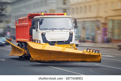 Snow Plow Utility Truck Riding On City Street, Municipal Services Preparing For Winter. Tipper With Plow, Heavy Industrial Machinery For Removing Snow And Clearing Snow Drifts