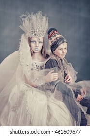 Snow Queen stole Kai. The young very beautiful girl in an elegant silver dress and make-up in a cold Snow Queen sits on a chair. He holds a very handsome boy in a suit Kai .