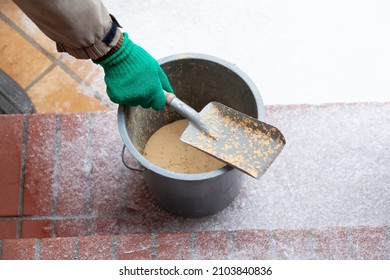 Snow and sand. A hand in a green glove holds a small spatula over a plastic sand bucket. Sand adhered chaotically on the scoop. White sand lies all around - Shutterstock ID 2103840836