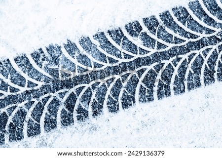 Snow tyre mark. Asphalt covered in snow. Dangerous road conditions. Car imprint on frozen ground. Tire trail on ice. City streets covered in snow during heavy snow fall. Slippery road background.