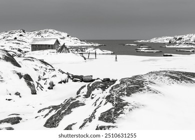 A snow-blanketed landscape of Bohuslän, Sweden showcases coastal cliffs and a quaint cabin. The serene, wintry scene captures the essence of winter by the sea. - Powered by Shutterstock