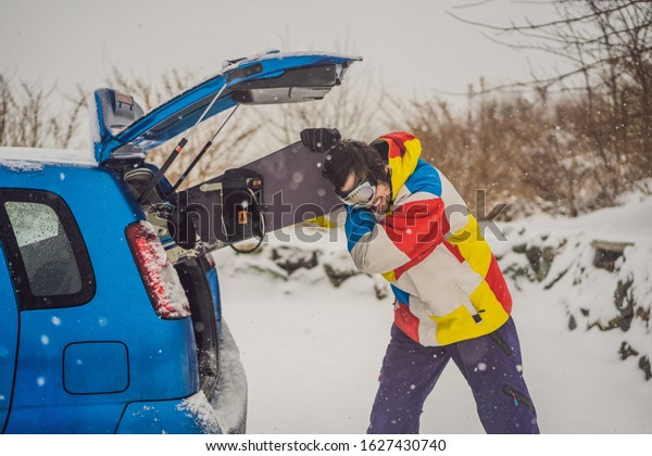 The snowboard\
does not fit into the car. A snowboarder is trying to stick a\
snowboard into a car. Humor,\
fun