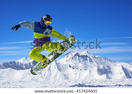 Snowboarder in bright sportswear doing trick against of beautiful mountains