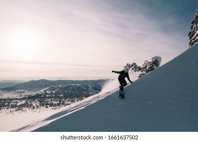 Snowboarder female riding on clear snow powder from steep slope, winter sunny day, free-riding in ski resort