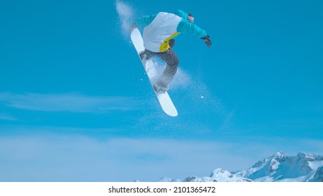 Snowboarder flies through the air and does a spinning nose grab while having fun in a snowpark in sunny Julian Alps. Awesome action shot of a man doing stunts while riding in Vogel snowboard park