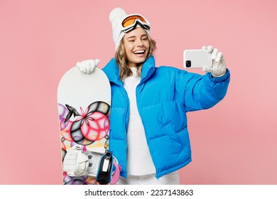 Snowboarder fun woman wear blue suit goggles mask hat ski padded jacket doing selfie shot on mobile cell phone isolated on plain pink background. Winter extreme sport hobby weekend trip relax concept - Powered by Shutterstock