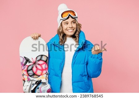 Snowboarder fun woman wear blue suit goggles mask hat ski padded jacket stand akimbo point aside on area isolated on plain pastel pink background. Winter extreme sport hobby weekend trip relax concept