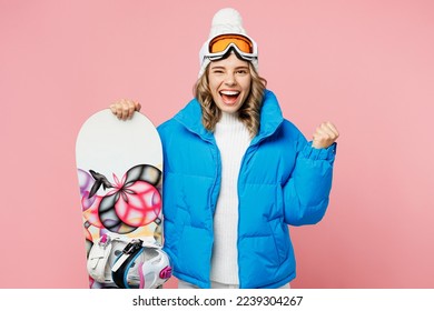 Snowboarder alegre mujer emocionada usa traje azul gafas máscara de gafas de máscaras de sombrero chaleco acolchado de esquí hace gesto de ganador aislado en un fondo rosa pastel claro. Concepto de relajación del viaje de fin de semana de hobby deportivo extremo invierno