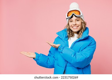 Snowboarder happy woman wear blue suit goggles mask hat ski padded jacket point arms hands aside on area isolated on plain pastel pink background. Winter extreme sport hobby weekend trip relax concept