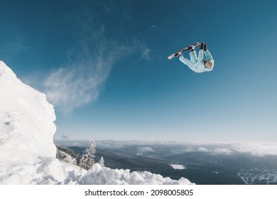 Snowboarder Making High Flip Big Air Jump In Clear Blue Sunny Sky Above Mountains