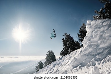 Snowboarder Making High Flip Big Air Jump In Clear Blue Sunny Sky Above Mountains