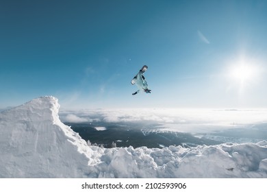 Snowboarder Making High Flip Big Air Jump In Clear Blue Sunny Sky Above Mountains