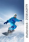 Snowboarder in retro blue outfit gliding smoothly, creating dynamic energy with snow flying against stunning snowy mountain backdrop. Concept of extreme sport, ski-resort, winter holidays. Ad