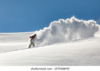 Snowboarder rides on fresh snow in the mountains against blue sky