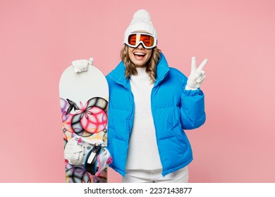 Snowboarder smilign cheerful woman wear blue suit goggles mask hat ski padded jacket show v-sign gesture isolated on plain pastel pink background. Winter extreme sport hobby weekend trip relax concept